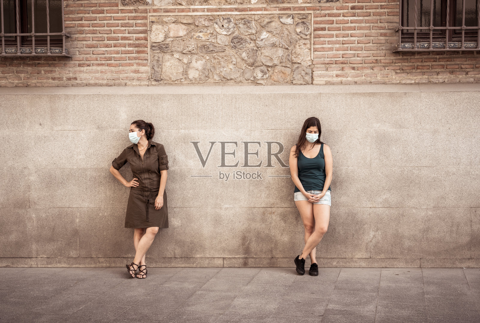 两名妇女戴着防护口罩，彼此站在2米远的地方保持社交距离，以避免冠状病毒的传播。新冠肺炎疫情防控与新常态的概念形象。照片摄影图片