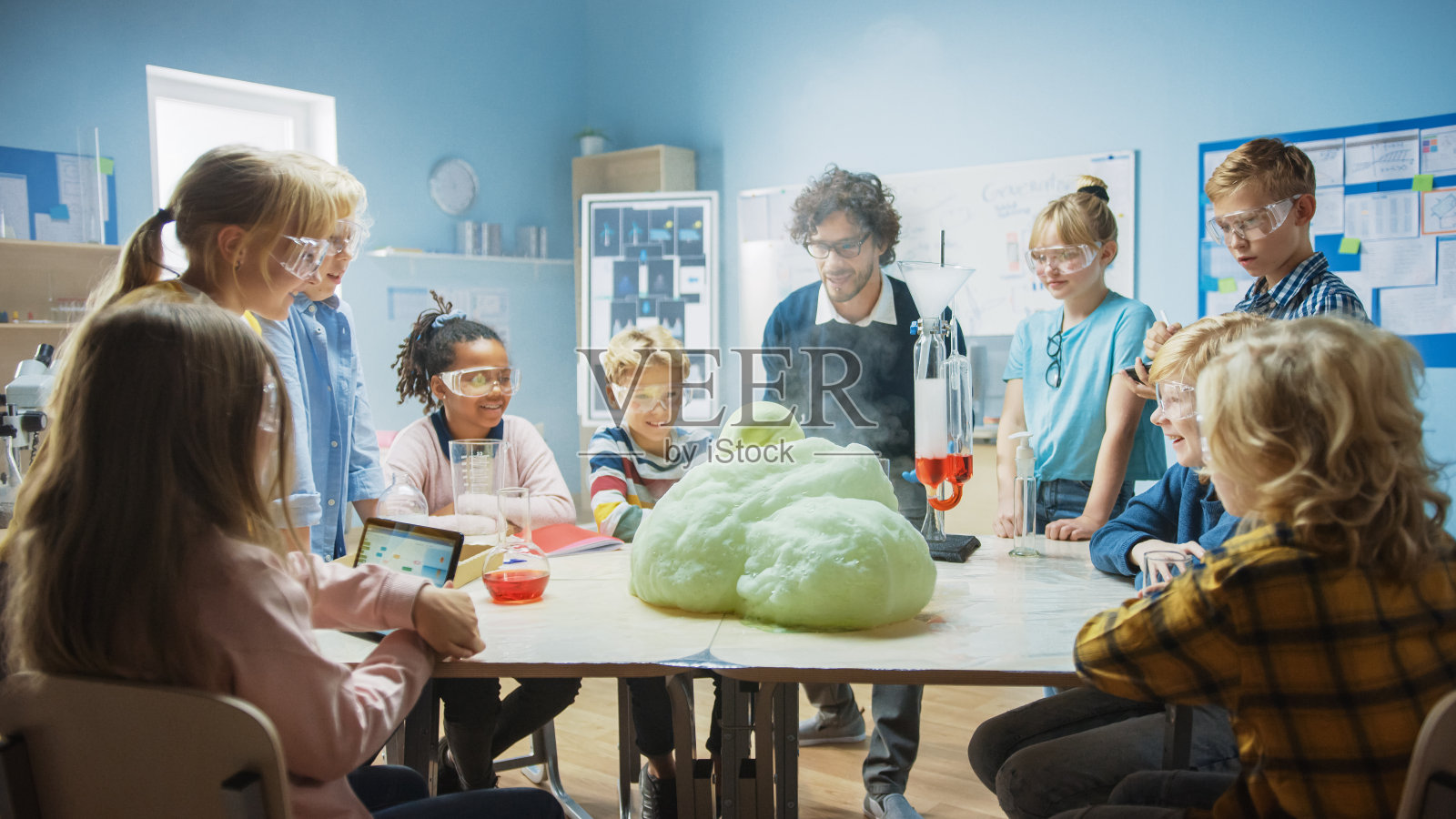 小学科学/化学课堂:热情的老师向小朋友展示有趣的化学反应实验。在烧杯中混合化学物质以喷射泡沫(大象牙膏)照片摄影图片