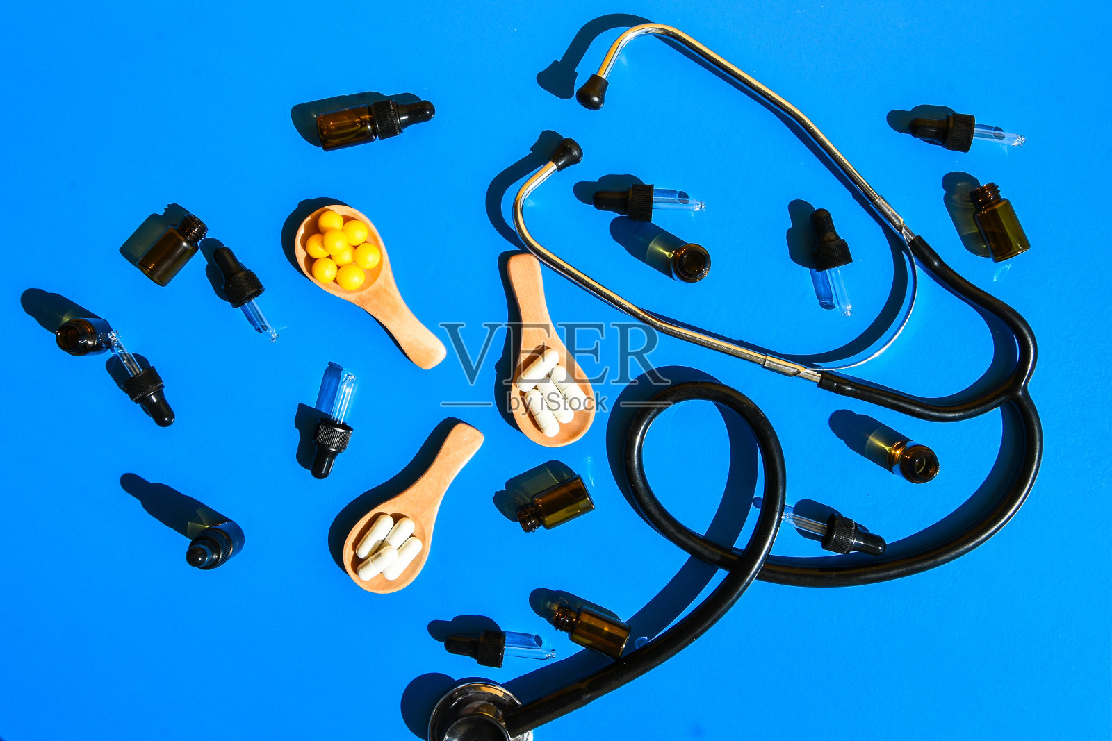 药片放在木勺和滴管上，声音内窥镜放在蓝色和黄色的背景上。强光和阴影。创造性的极简主义的概念。维生素和益生元，益生菌。剂量照片摄影图片