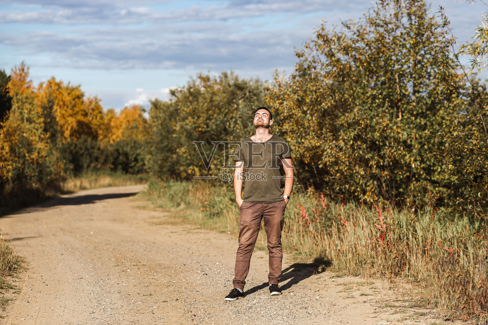 年轻快乐的英俊男子在秋天的公园里闭上眼睛深呼吸新鲜的空气在阳光明媚的秋天的一天。自然放松，人们梦想，幸福和健康的生活方式的概念照片摄影图片