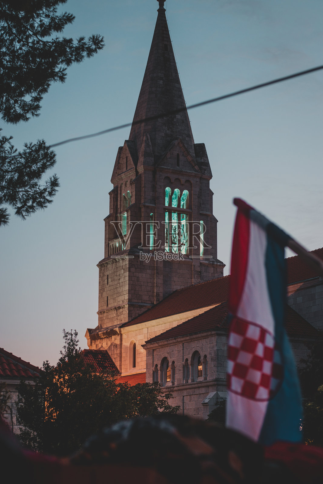 这是克罗地亚布拉克岛塞尔卡村一座古老教堂美丽的钟楼顶部。在克罗地亚国旗下，一个基督教标志性建筑在夜晚发光的蓝色垂直镜头照片摄影图片