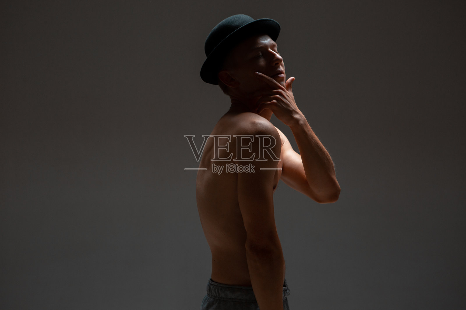 时尚的年轻人演员站在帽子没有衬衫在演播室孤立的黑色背景照片摄影图片