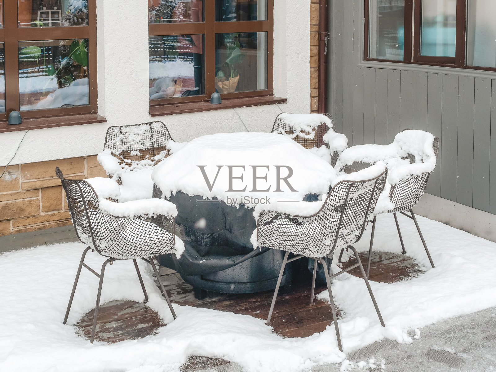 铺着深色床单的桌子，周围摆着几把椅子，放在撒满雪的窗户下面照片摄影图片