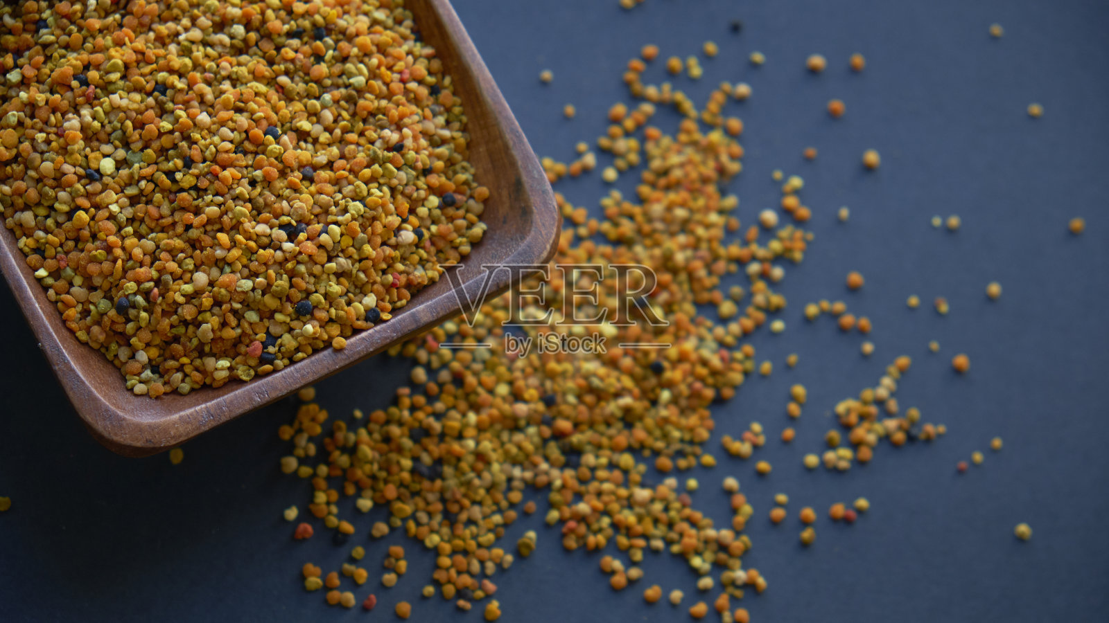 木勺里的蜂花粉是健康食品的补充。黑色表背景。工蜂从地里采集的花粉的球状或小球照片摄影图片