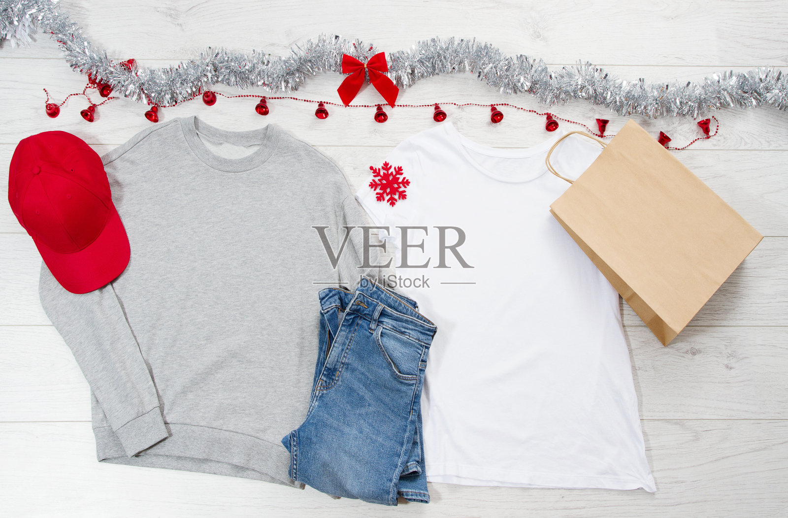 关闭白色空白模板t恤，运动衫连帽衫与复制空间。圣诞假期的概念。顶视图纸包t恤，红色的帽子上白色的木制背景。新年装饰品照片摄影图片