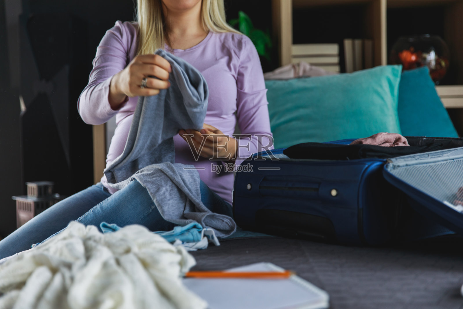 期待着妈妈坐在床上，把衣服装进行李箱照片摄影图片