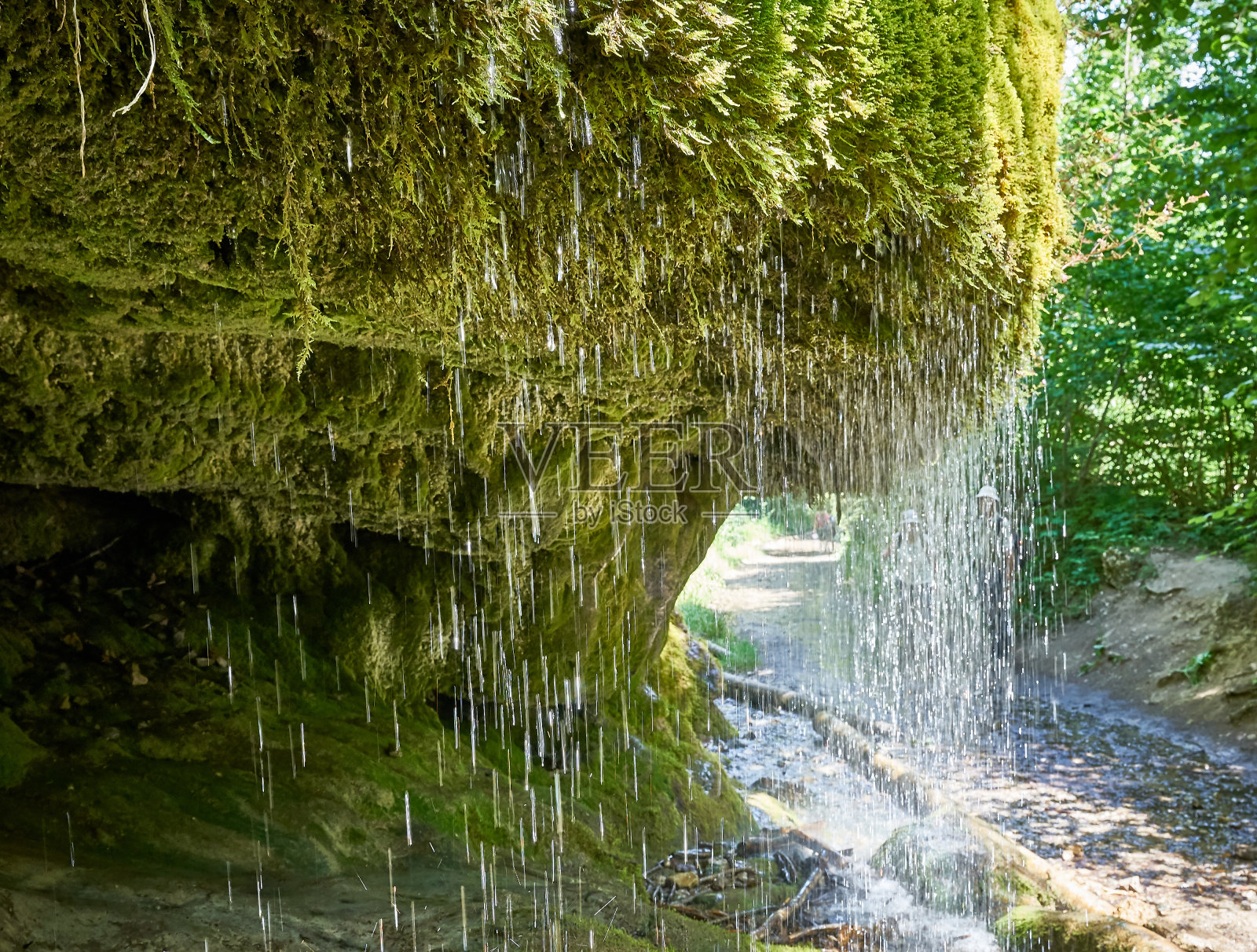 瀑布流过长满苔藓的岩石，后面有洞穴照片摄影图片