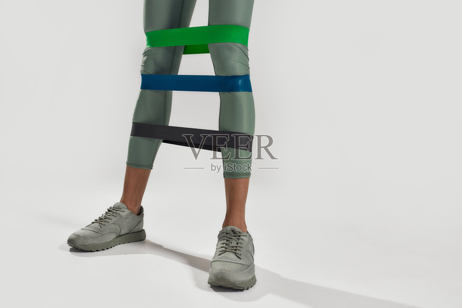 更强的腿。近距离的运动妇女做腿部运动使用健身口香糖，三个橡皮筋隔离在灰色背景。健康的生活方式和运动理念照片摄影图片