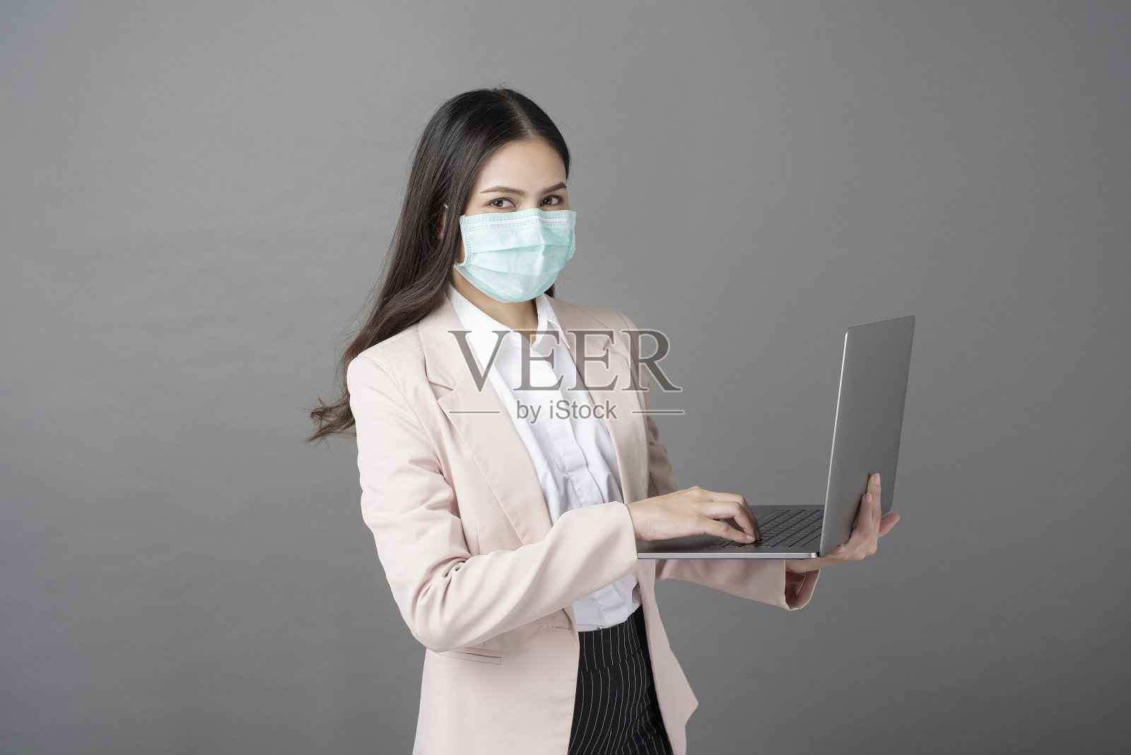 带着外科口罩的女商人正拿着笔记本电脑照片摄影图片