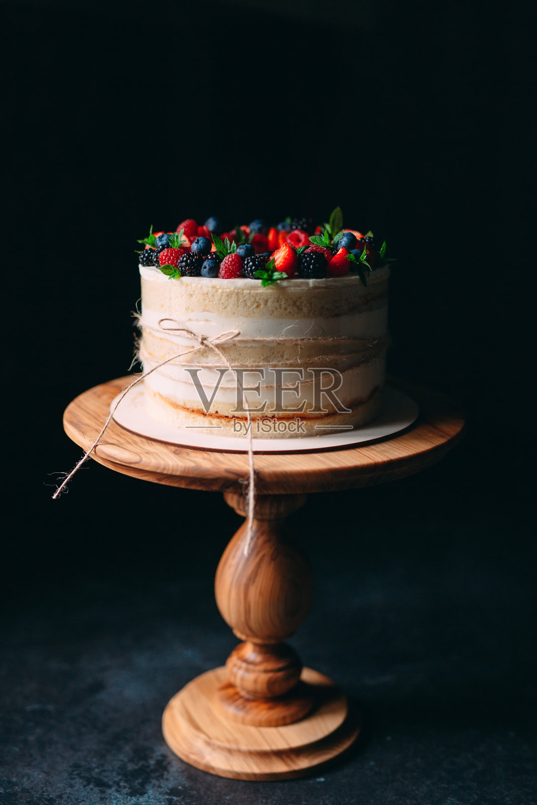 水果蛋糕。用浆果装饰的蛋糕，放在黑色背景的木架上。照片摄影图片