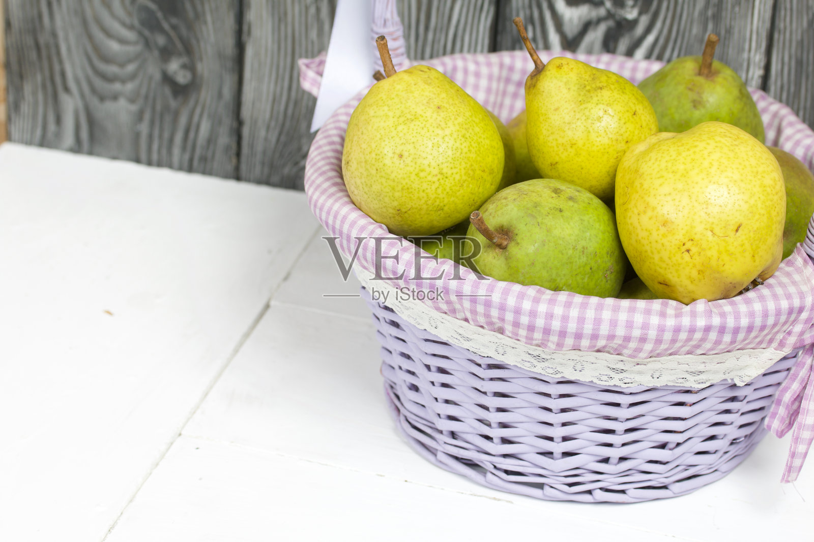 柳条篮子里装着新收获的熟透的梨。以涂了漆的松木板为背景。照片摄影图片