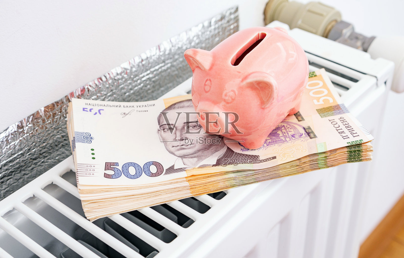 家里暖气片上有乌克兰钱的存钱罐。支付公用事业服务，节能房，概念形象。照片摄影图片