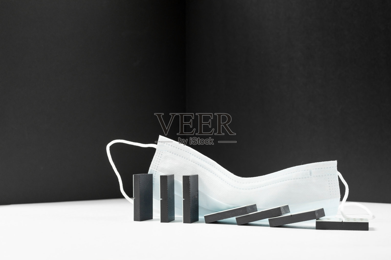 黑多米诺倒下了，站在白色的背景上，带着医用面具。商业危机、因冠状病毒大流行而破产的概念。副本的空间。照片摄影图片