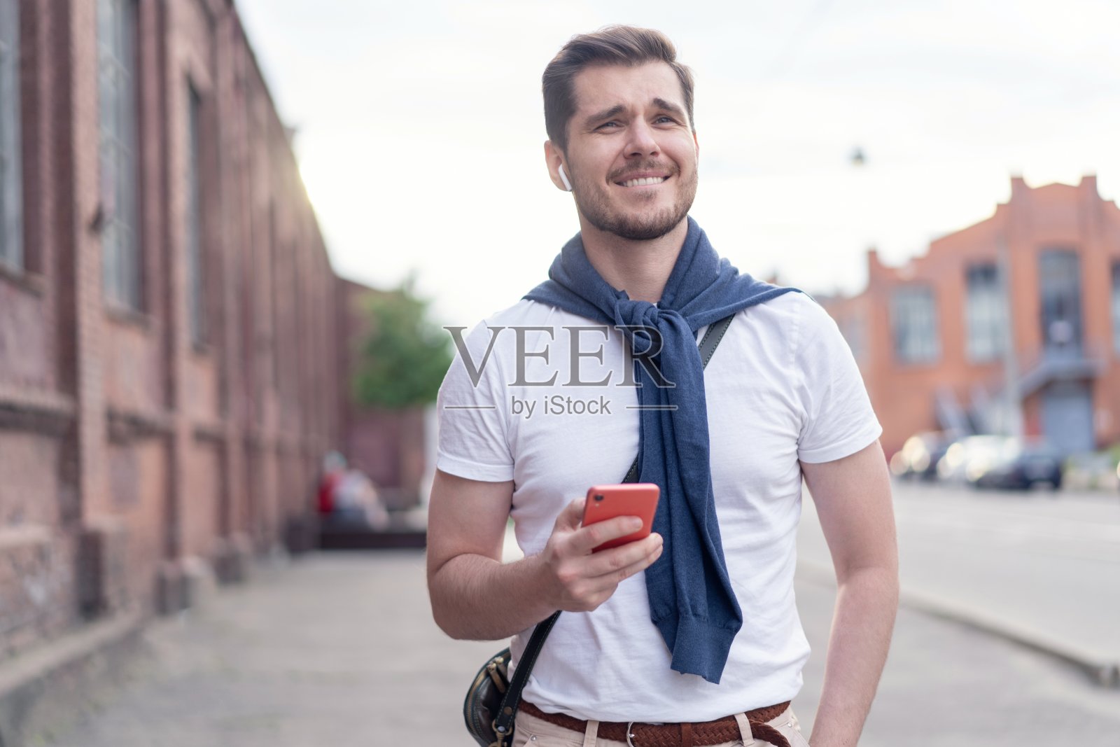 英俊微笑的男人一边听音乐一边走在城市里照片摄影图片