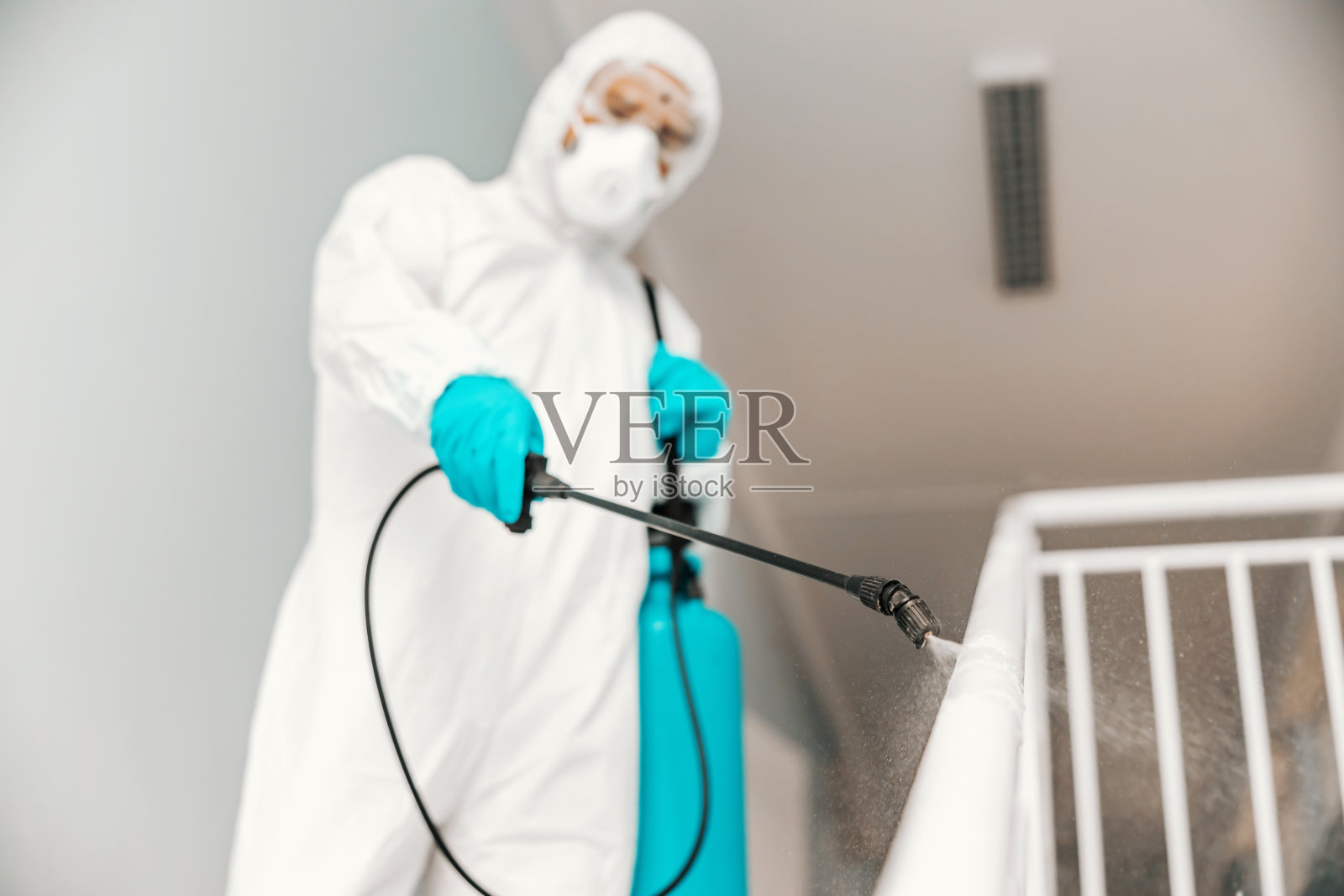 特写工作人员在无菌制服，与手套和口罩消毒栏杆在学校。选择性地使用喷雾器。照片摄影图片