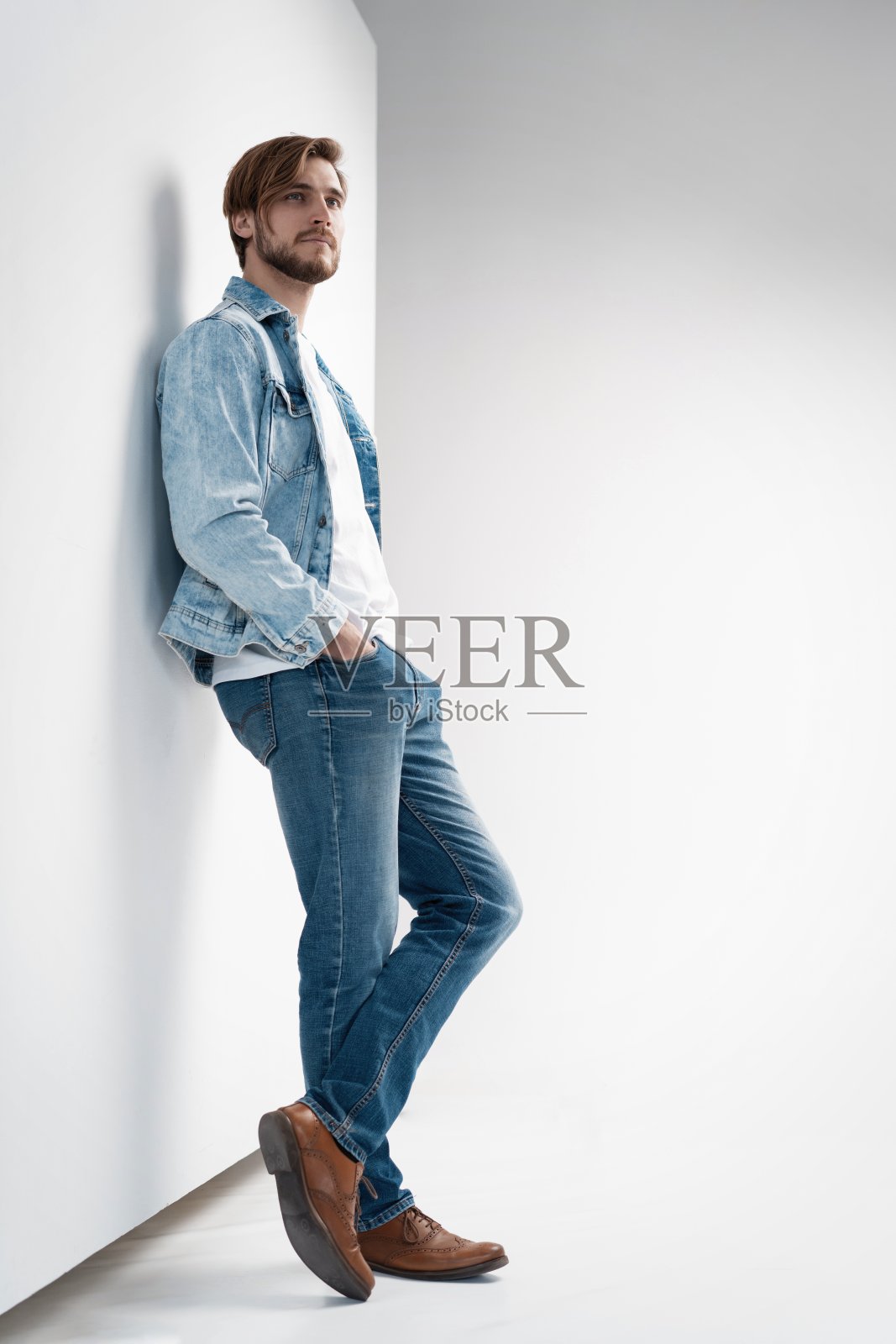 年轻男子穿着牛仔裤夹克的时尚肖像。照片摄影图片
