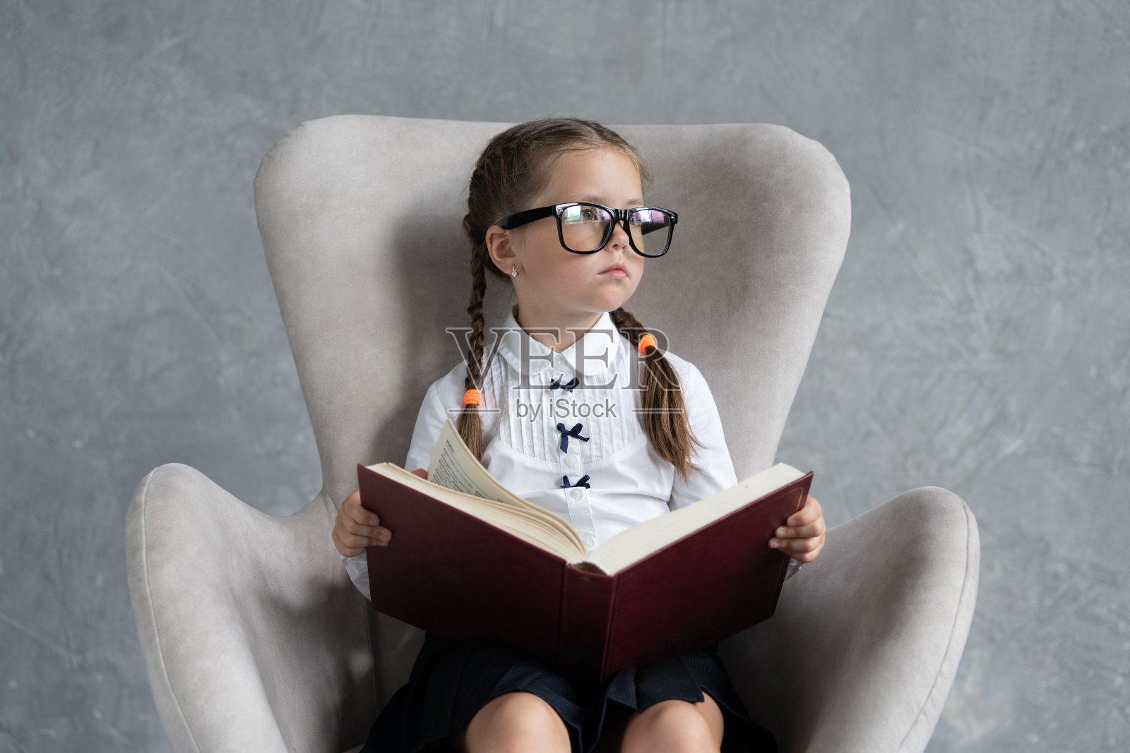 女学生坐在扶手椅上专心看书。照片摄影图片