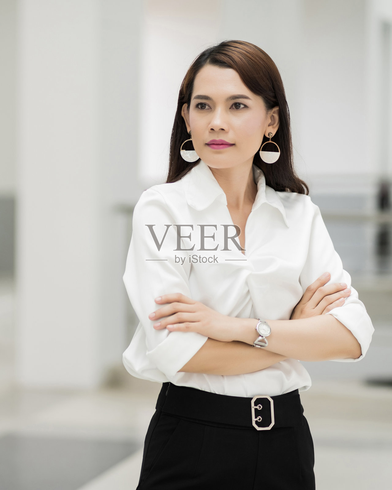 一个快乐的中年女商人穿着商务套装，双臂交叉站在公司大楼里。现代商业女性在有复印空间的办公室。商业女性获得stoc照片摄影图片