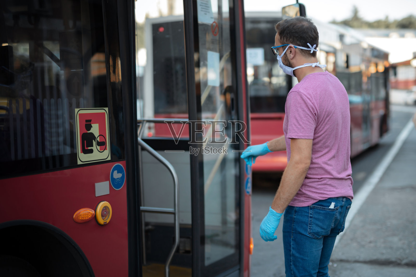 一名戴着医用防护口罩和手套的男子在公共交通车站进入公共汽车。照片摄影图片