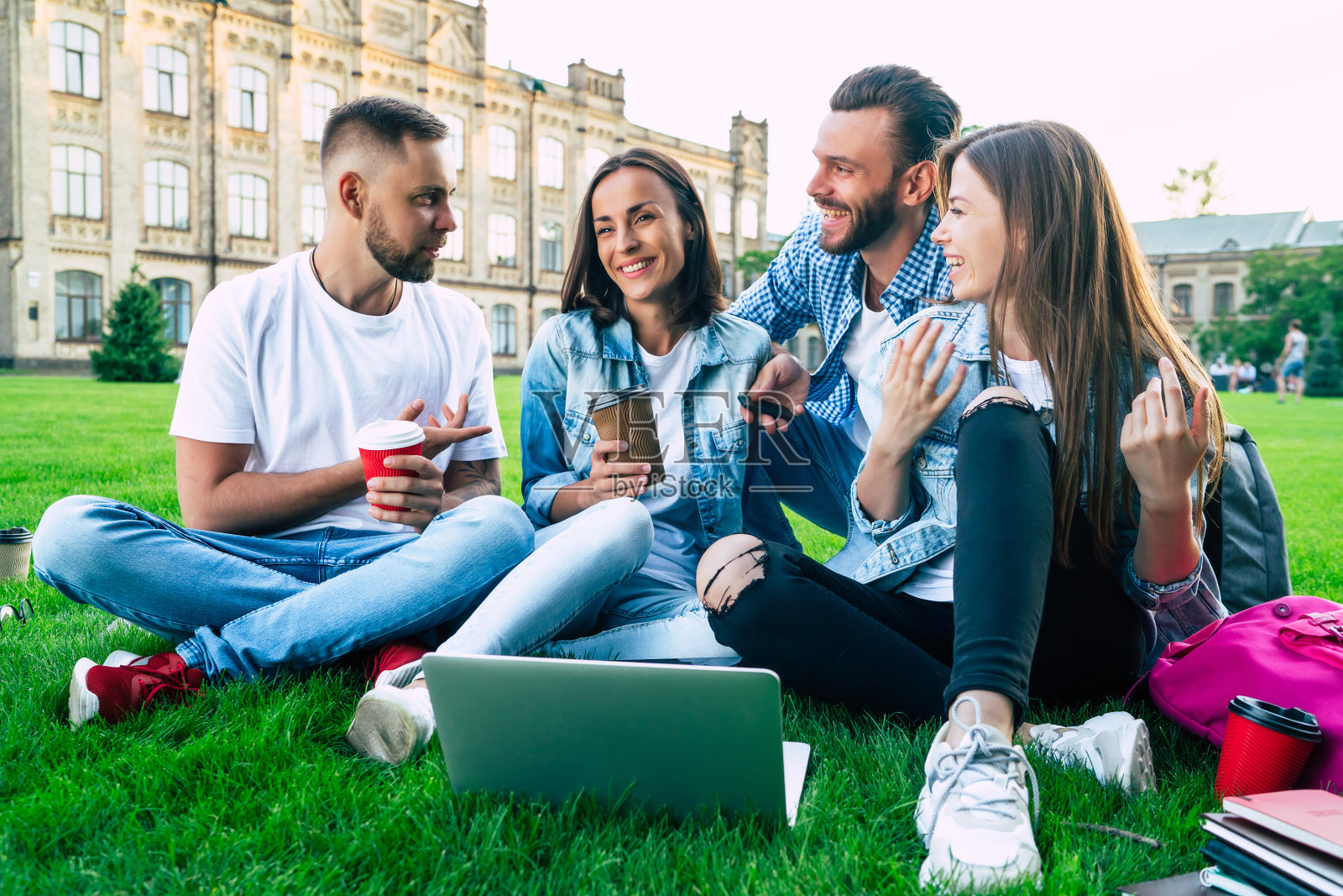 四个最好的年轻学生朋友拿着一台笔记本电脑，在大学地盘的草地上快乐而兴奋照片摄影图片