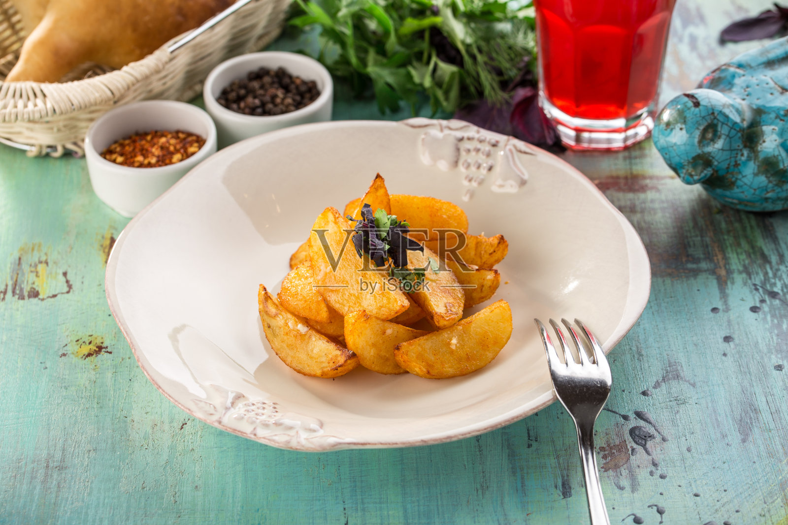 白色的盘子上放着烤土豆，蓝色的木桌上放着一杯红色的饮料照片摄影图片