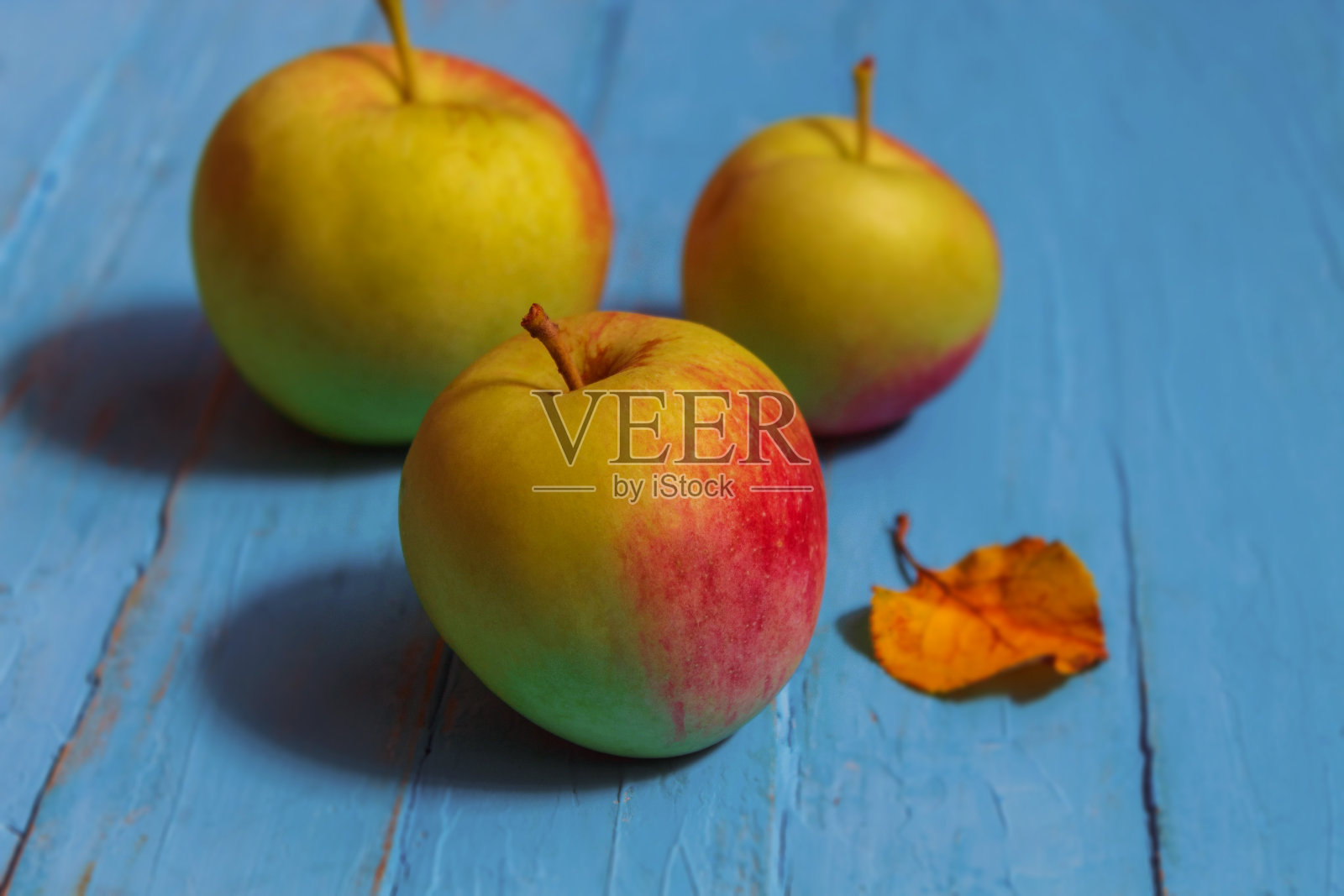 三个新鲜的苹果放在一张木头桌子上，旁边有一片小树叶照片摄影图片