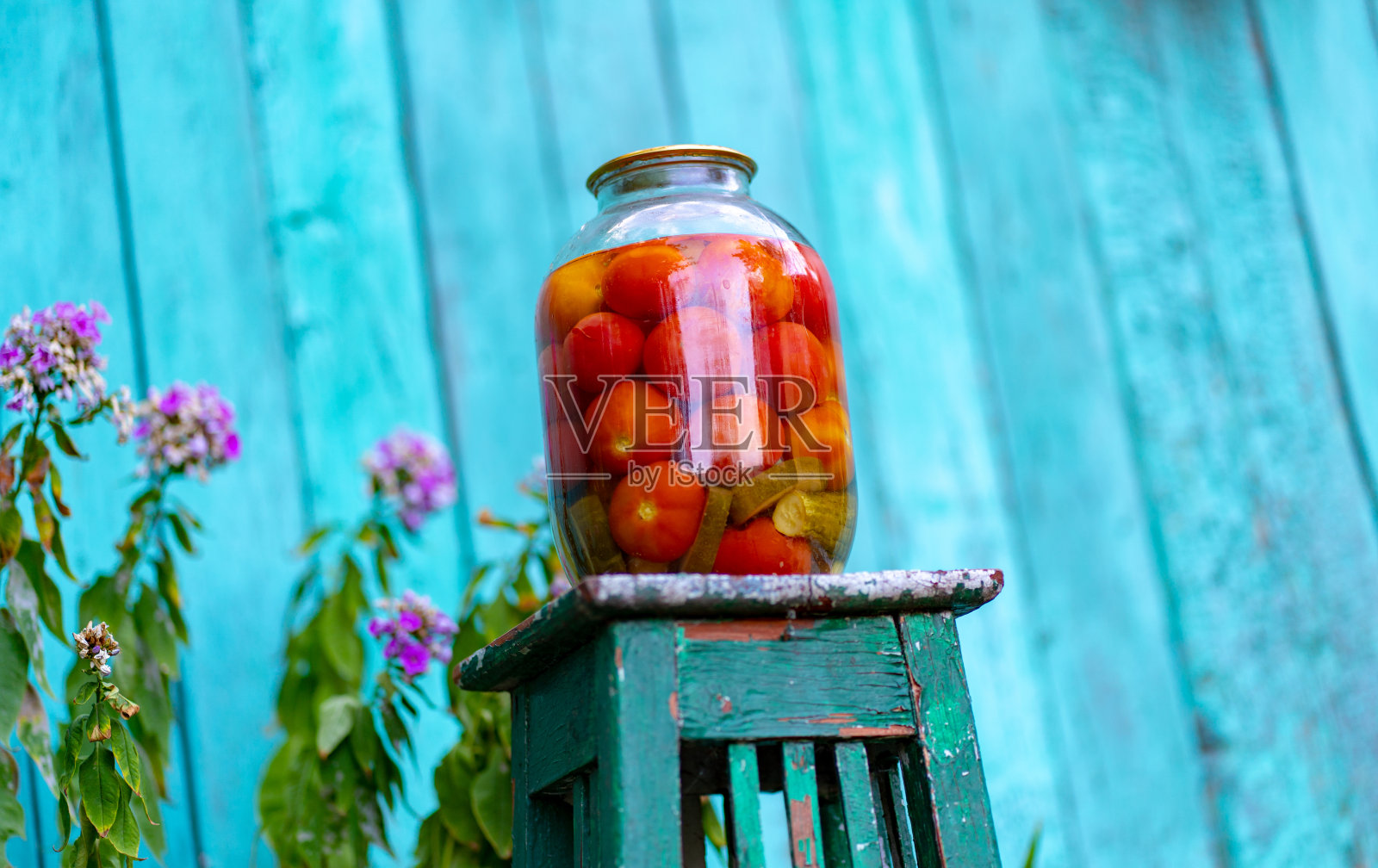 椅子上放着一个大玻璃瓶，里面放着腌菜，背景是老木屋。花园里的街道上，用密封的罐子装着番茄和黄瓜罐头照片摄影图片