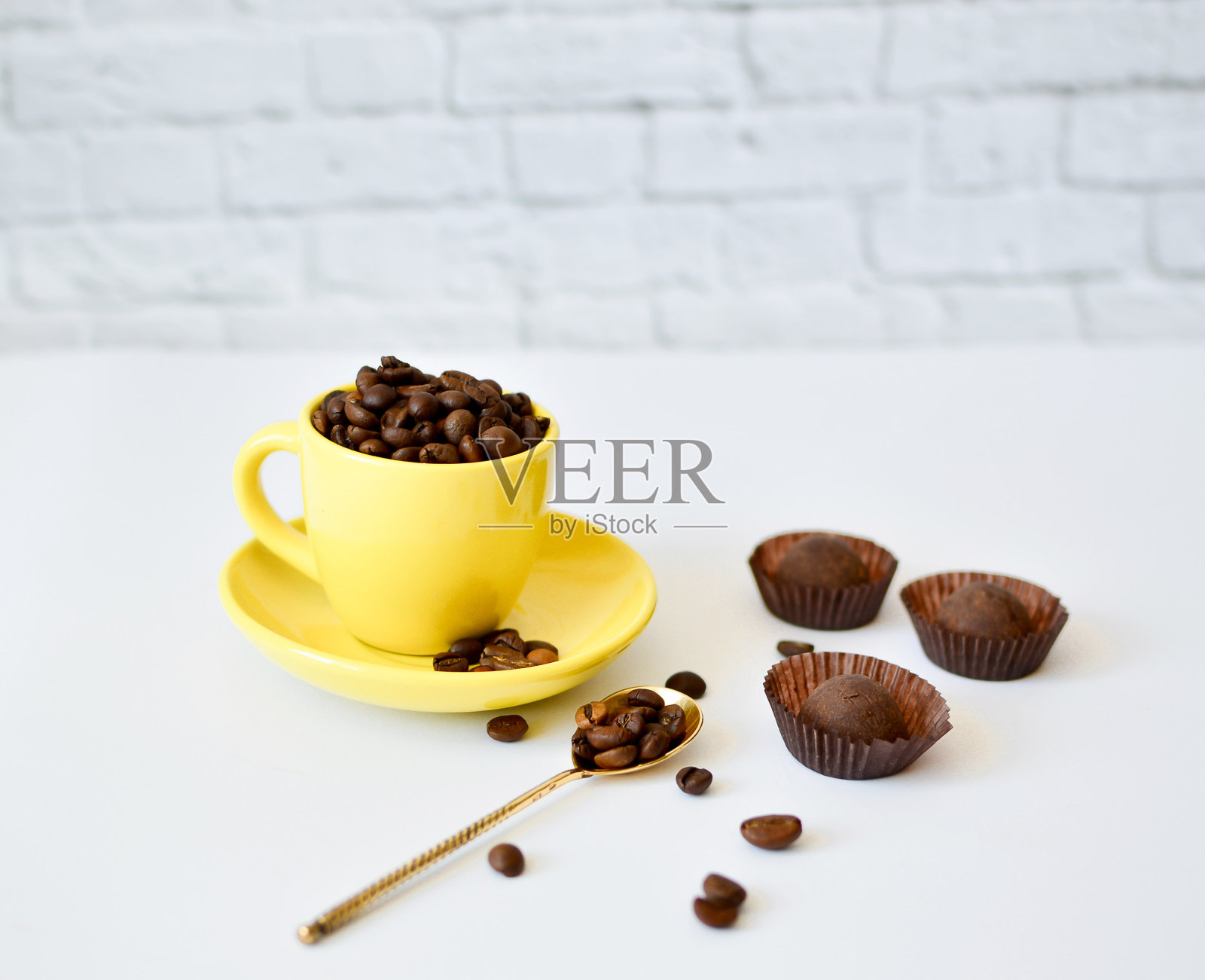 一个黄色的杯子，上面有天然的咖啡豆，白色的背景，还有巧克力。早上咖啡的概念。背景上有花。照片摄影图片