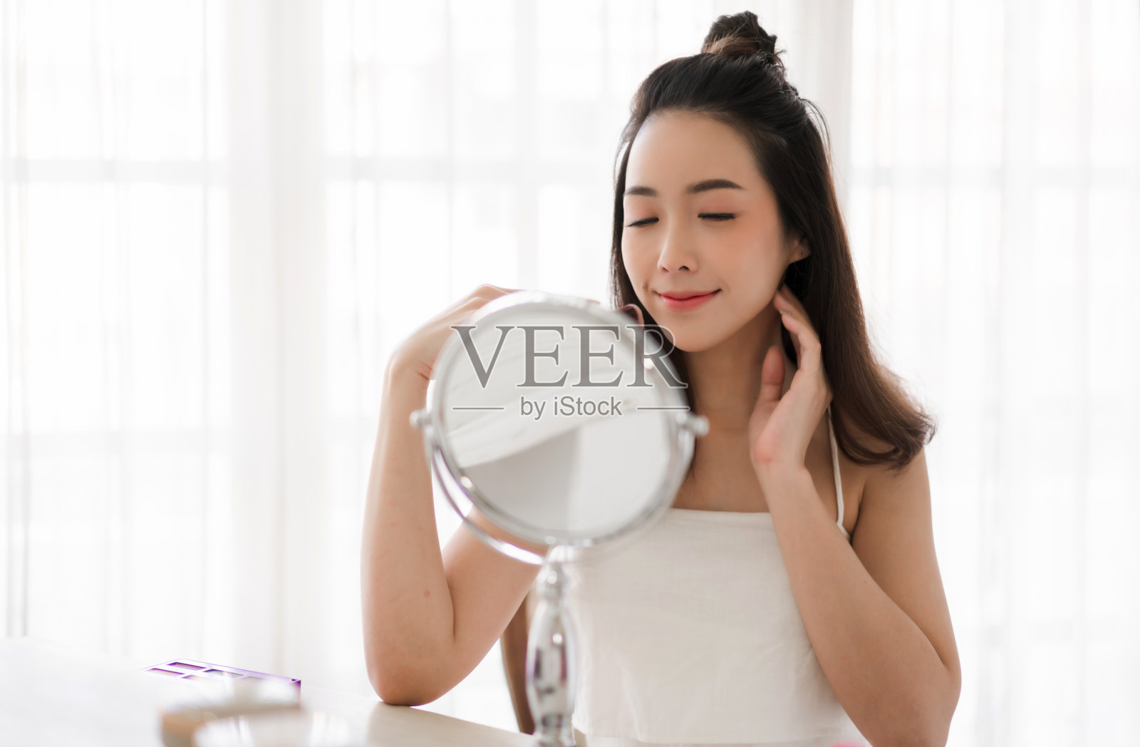 微笑年轻美丽的女人，新鲜健康的皮肤看着镜子，化妆化妆在家。面部美容和化妆概念照片摄影图片