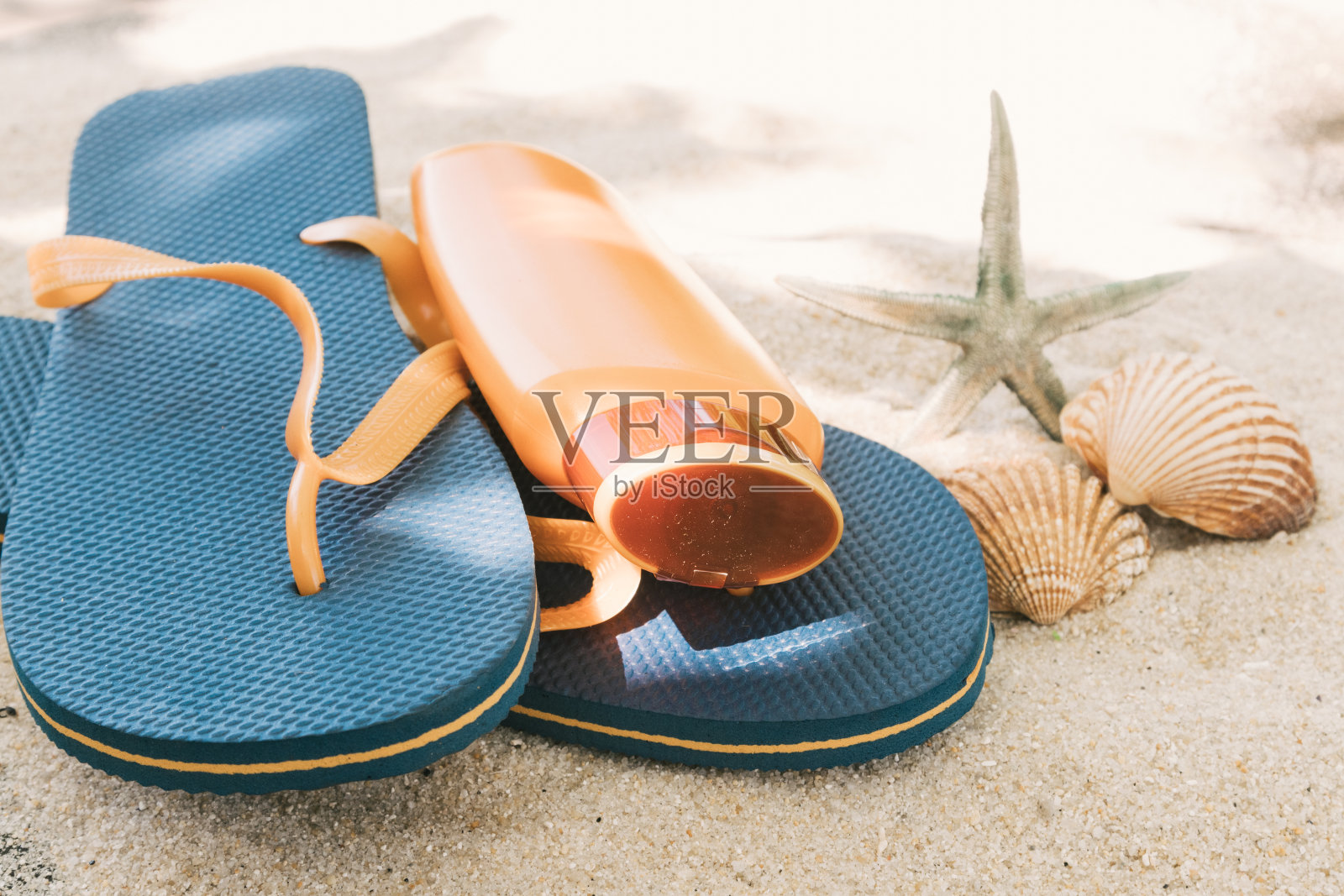 一瓶防晒油或防晒霜放在沙滩上，上面有海贝照片摄影图片