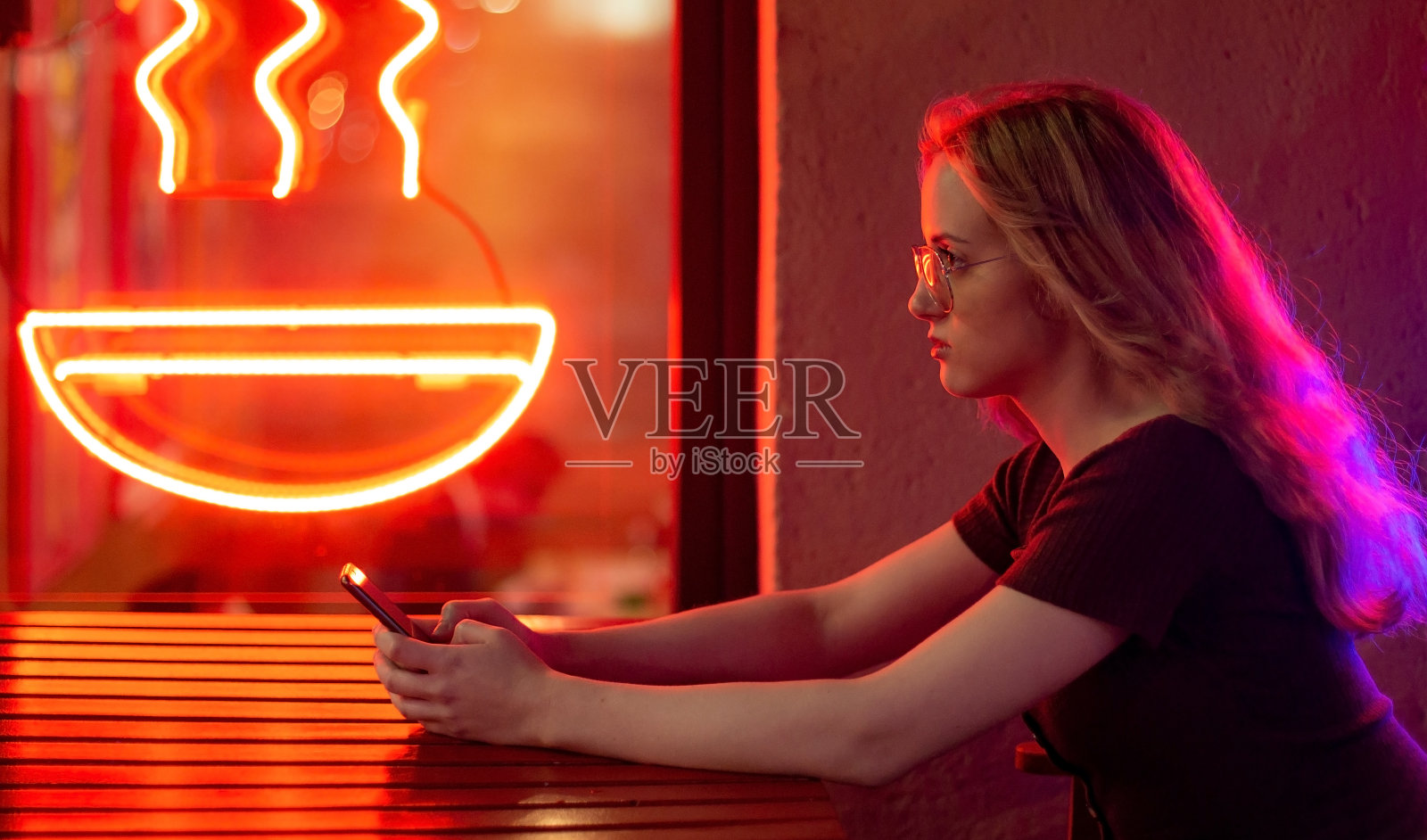 一个年轻快乐的女人坐在户外咖啡馆在晚上使用手机。照片摄影图片