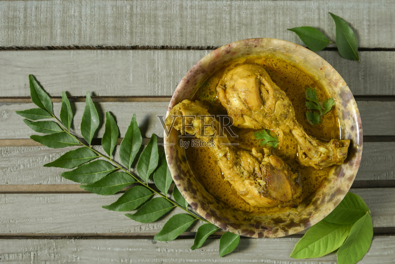 咖喱鸡或香料，辣红鸡腿片配香菜叶，安排在一个白色陶瓷碗与木制背景照片摄影图片