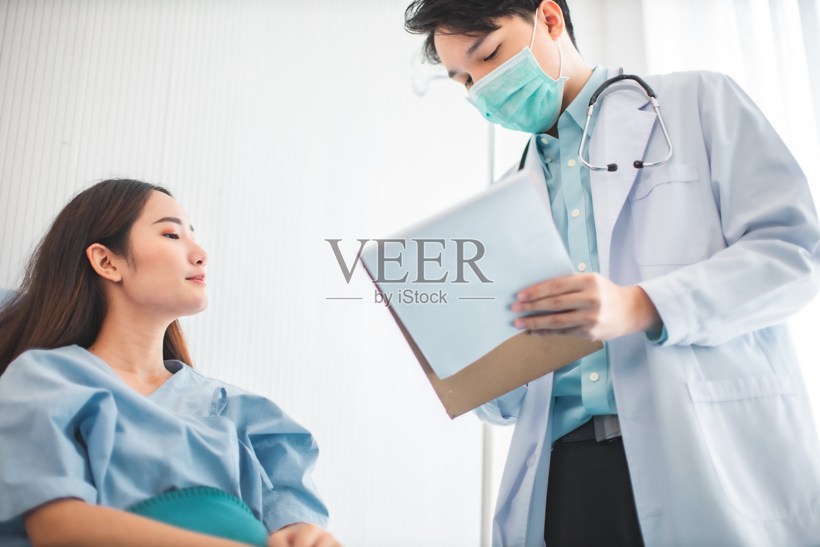 医学保健理念。一位亚洲医生正在医院里照顾一位女病人。医生或护士佩戴防护口罩检查和护理COVID-19感染者。照片摄影图片