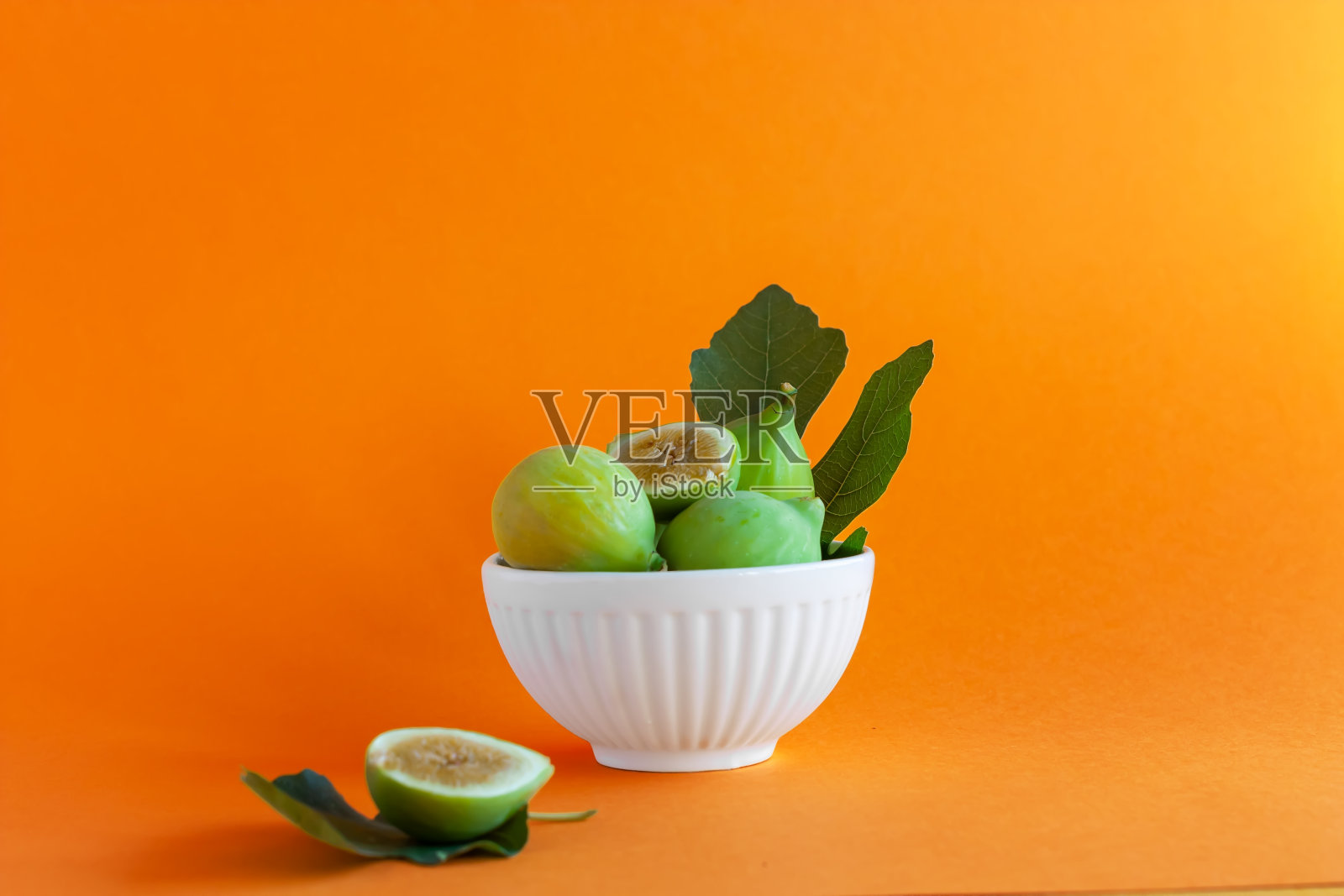 白色瓷碗里盛着成熟的无花果叶，橙色背景。收获与健康的饮食理念。有选择性的重点照片摄影图片