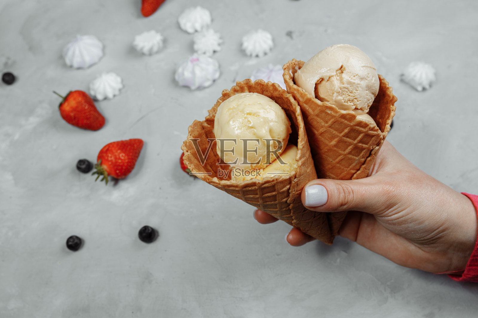 冰激淋在华夫蛋筒上在一个轻的背景在一个手。冰淇淋正在融化。背景是华夫饼和草莓照片摄影图片