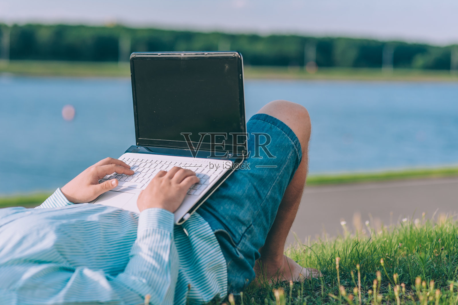 一个戴眼镜、穿衬衫的男人在新鲜的空气中用笔记本电脑工作，背景是一条河。照片摄影图片