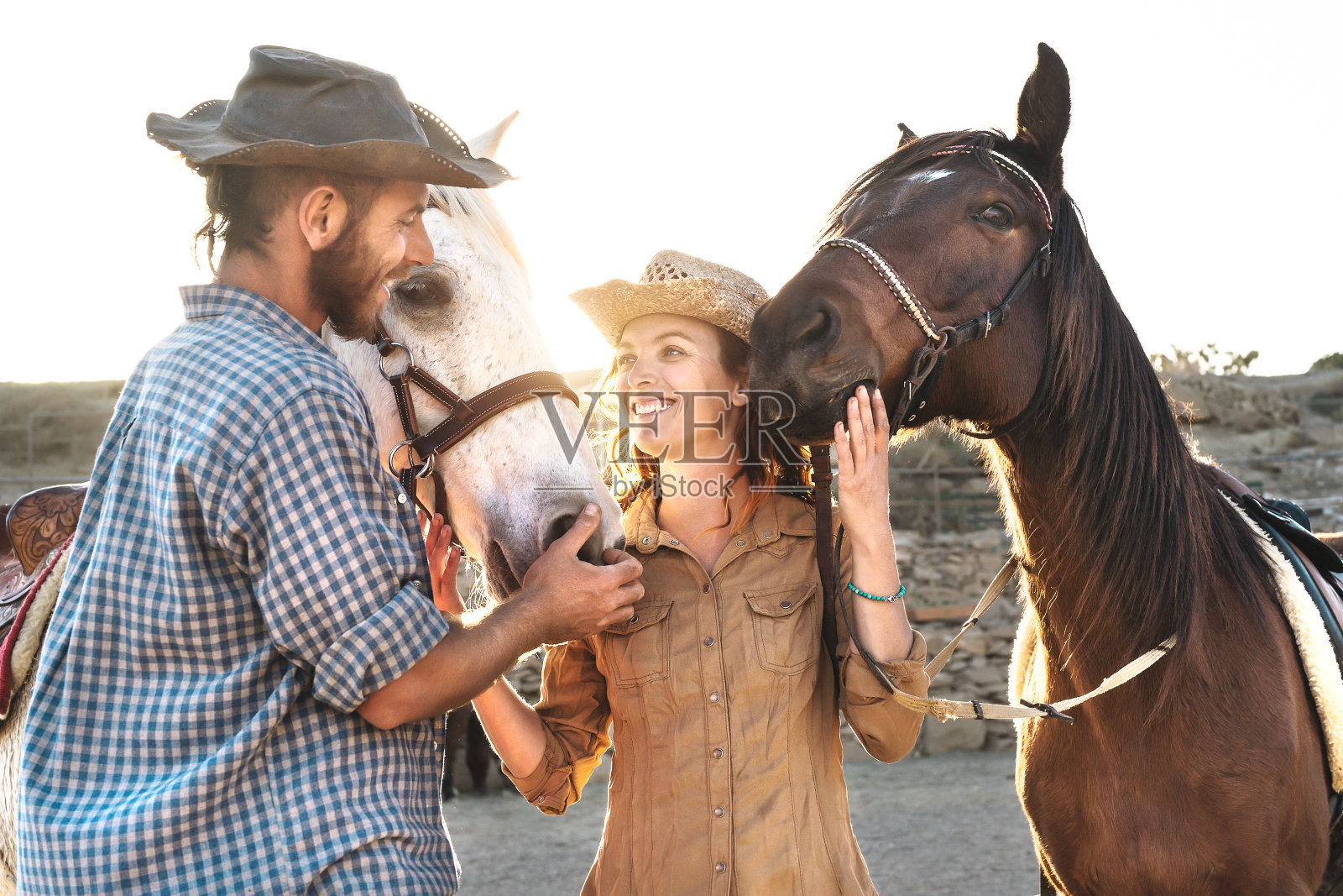 快乐的夫妇与马在马厩里玩-年轻的农民分享时间与动物在畜栏牧场-人类和动物关系的生活理念照片摄影图片
