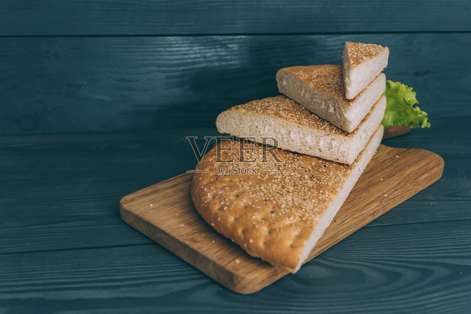 灰色桌子上的切菜板上的绿叶面包。照片摄影图片