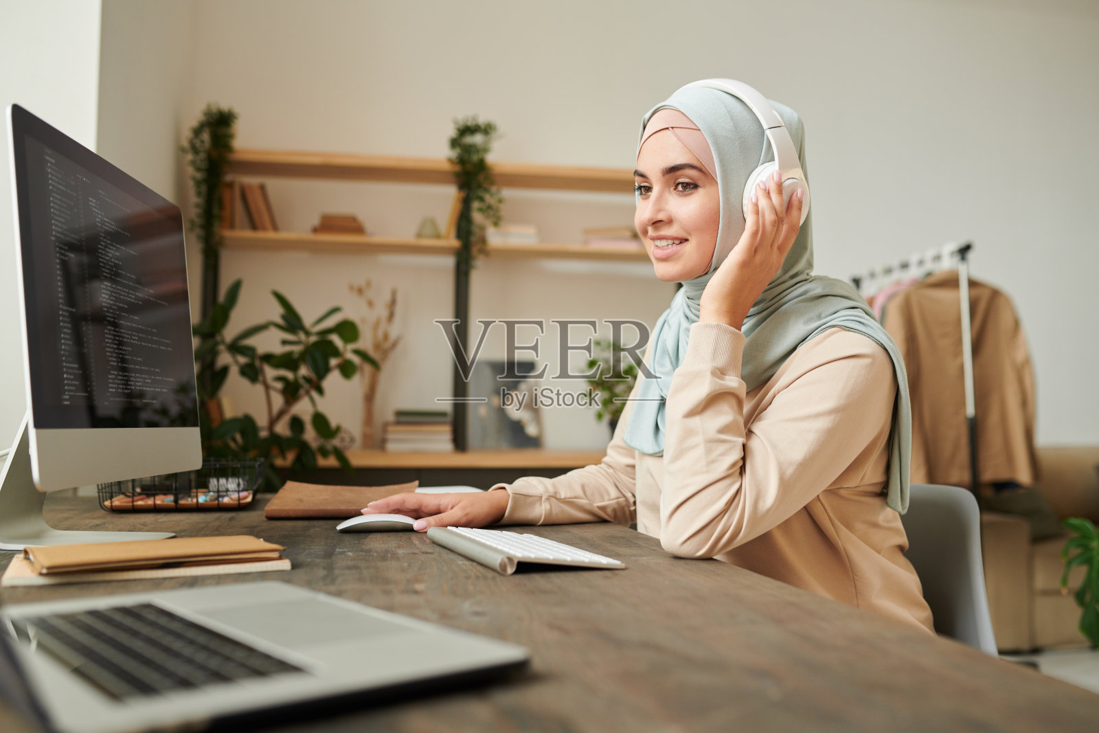 肖像的专业软件开发人员戴着头巾和耳机坐在桌子上进行在线会议，同时在电脑上工作照片摄影图片
