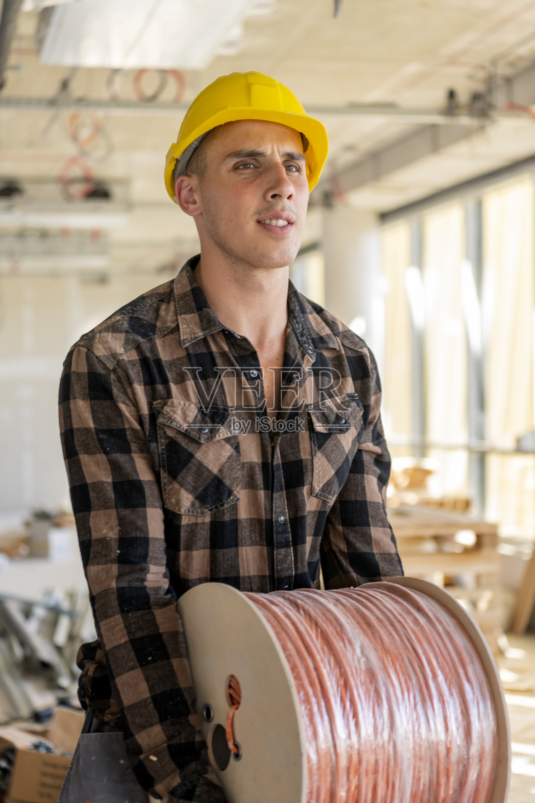 电工戴着安全帽，穿着制服，手里拿着一卷电缆照片摄影图片