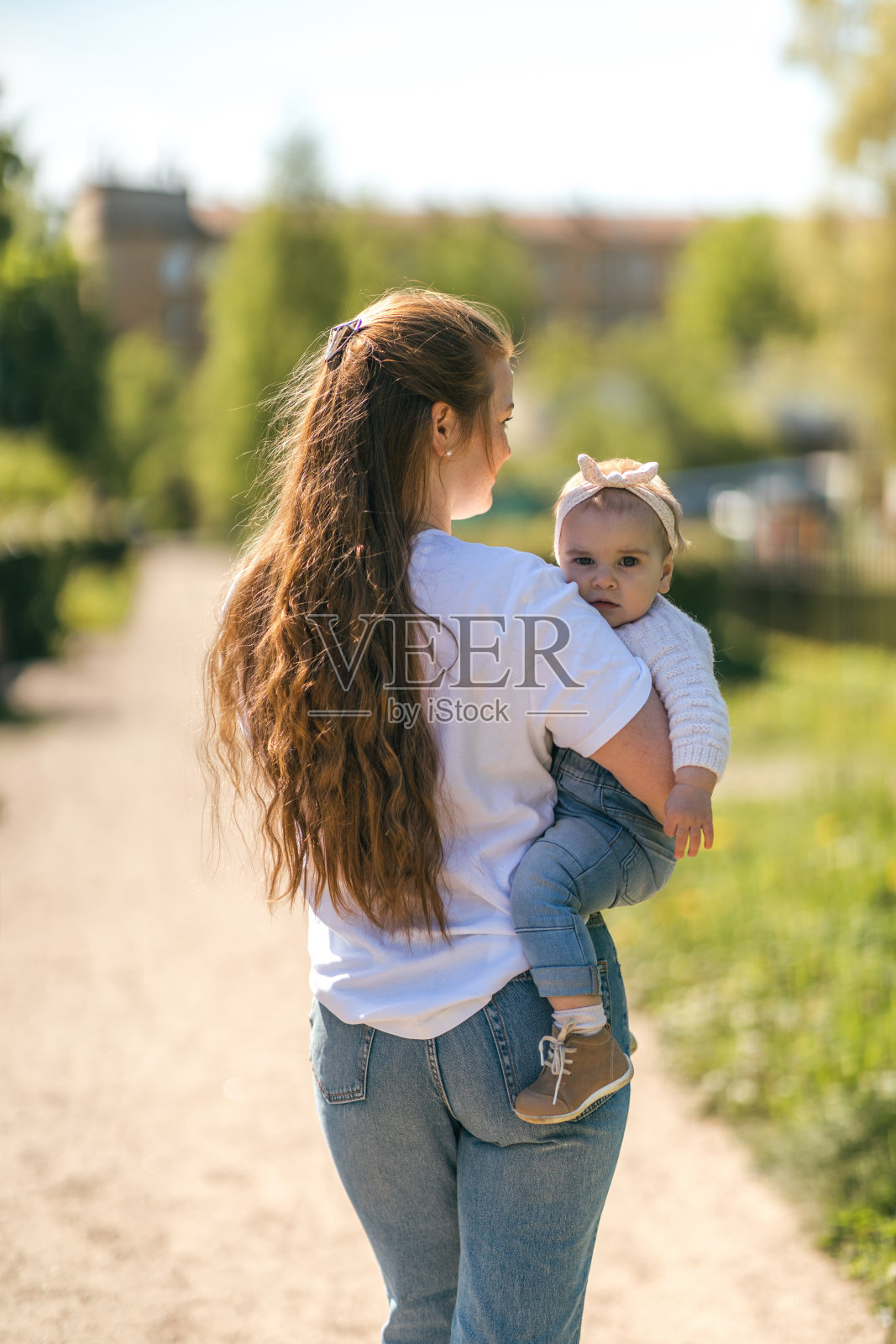 一个年轻的妈妈带着一个一岁的婴儿走，把他抱在怀里，拥抱。与孩子沟通，让他和谐发展照片摄影图片