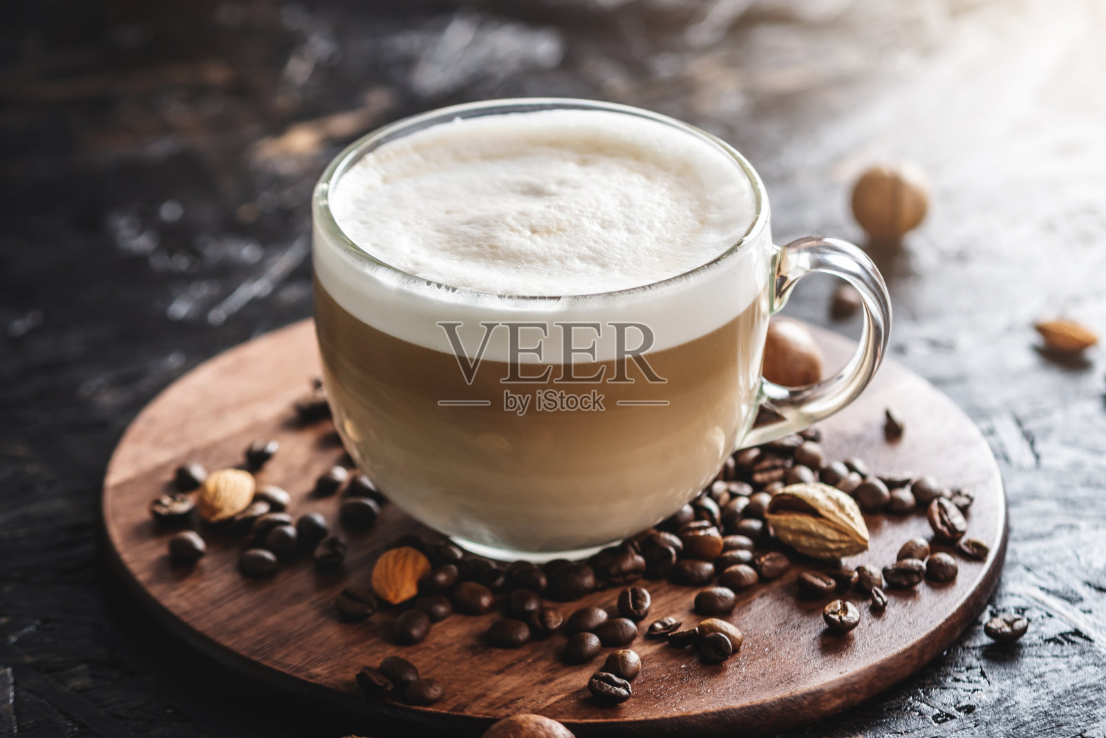 香喷喷的拿铁放在一个透明的杯子里，放在一个棕色的木托盘上。附近有咖啡豆和坚果。早餐或在舒适的咖啡馆喝咖啡休息照片摄影图片