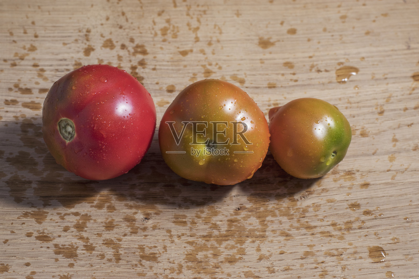 厨房的白橡木板上放着三个不同成熟度的湿西红柿。照片摄影图片