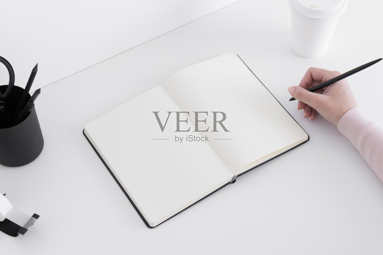 打开笔记本模型，咖啡纸杯，白色桌子上的工作区配件，女人在做笔记。照片摄影图片