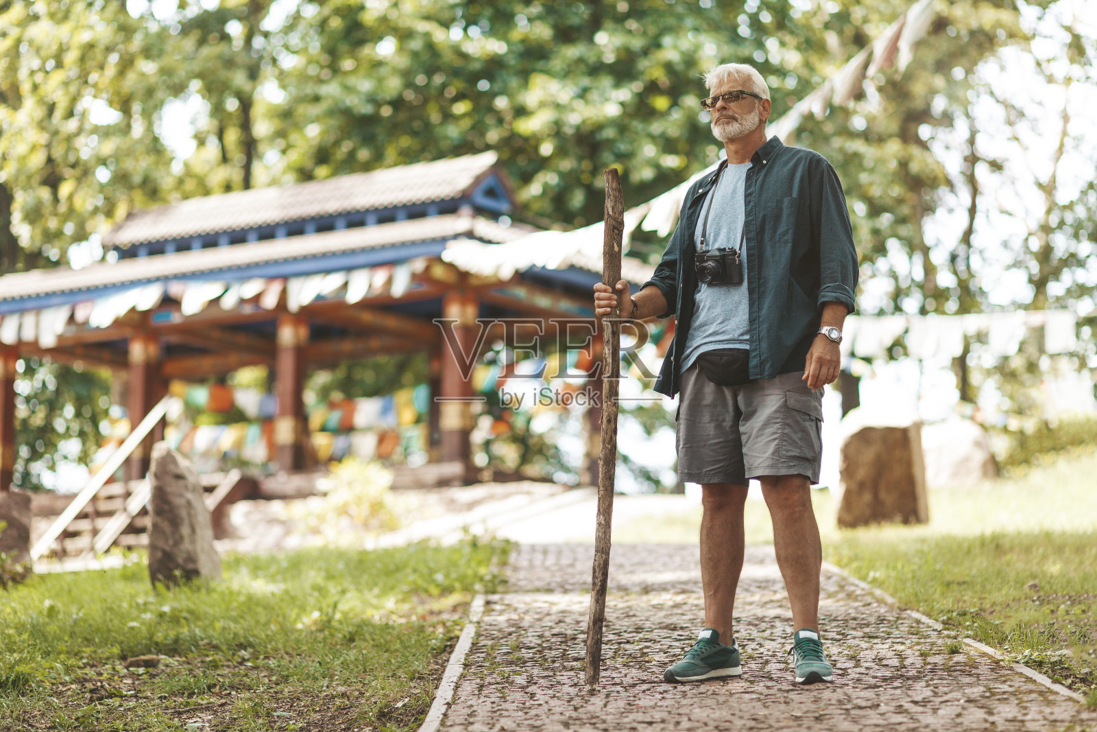 一位欧洲老人和游客拄着拐杖站在一座佛教寺庙的背景下。去修道院进行宗教朝圣。前往权力的圣地照片摄影图片