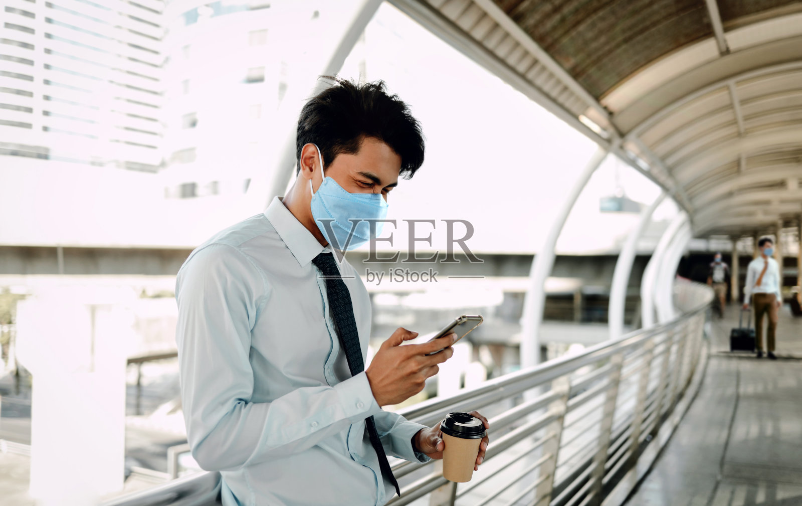 年轻的亚洲商人戴着外科口罩，在城市里使用智能手机。新常态生活理念下的医疗保健照片摄影图片