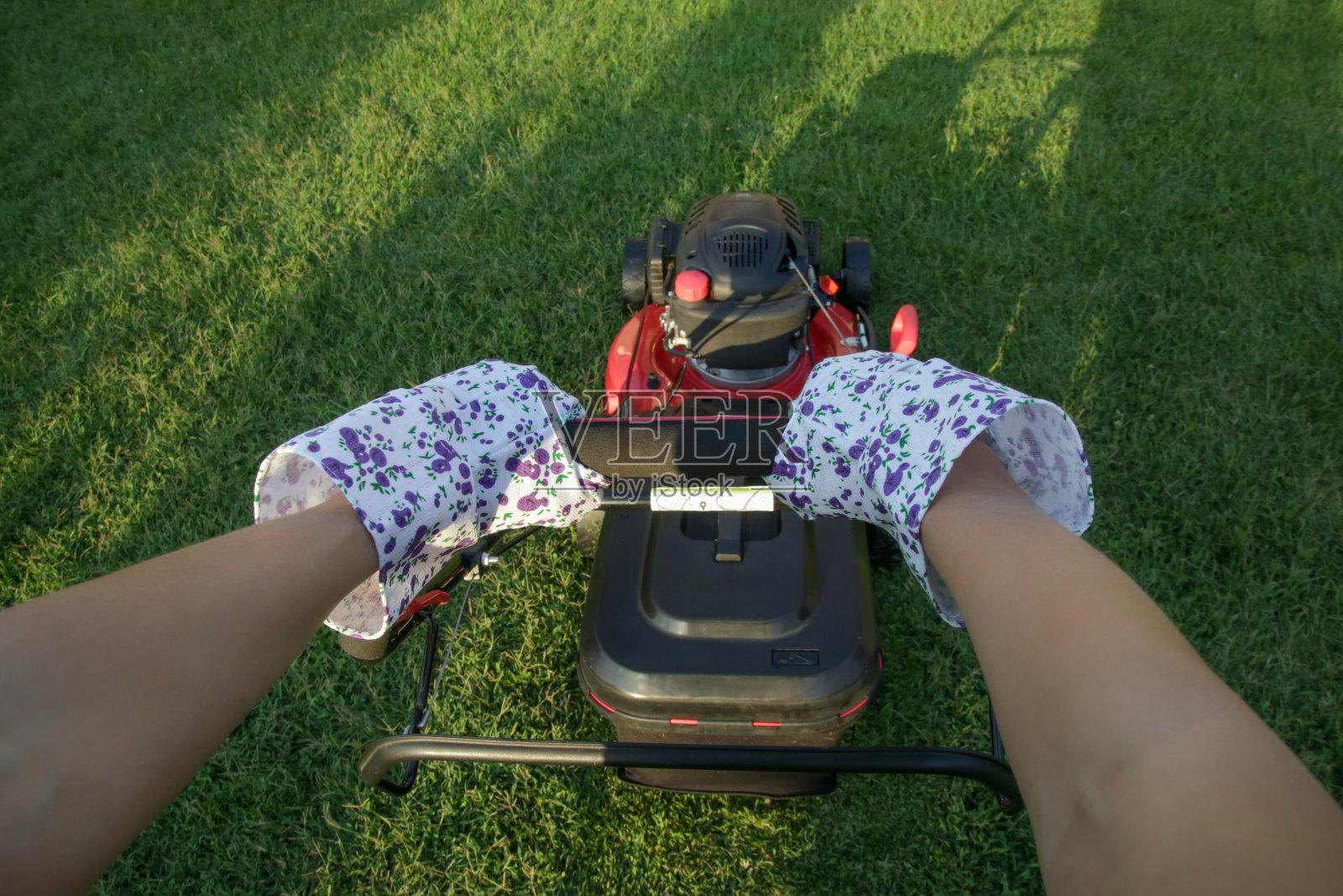 用割草机割草的年轻女子。户外家务概念。照片摄影图片