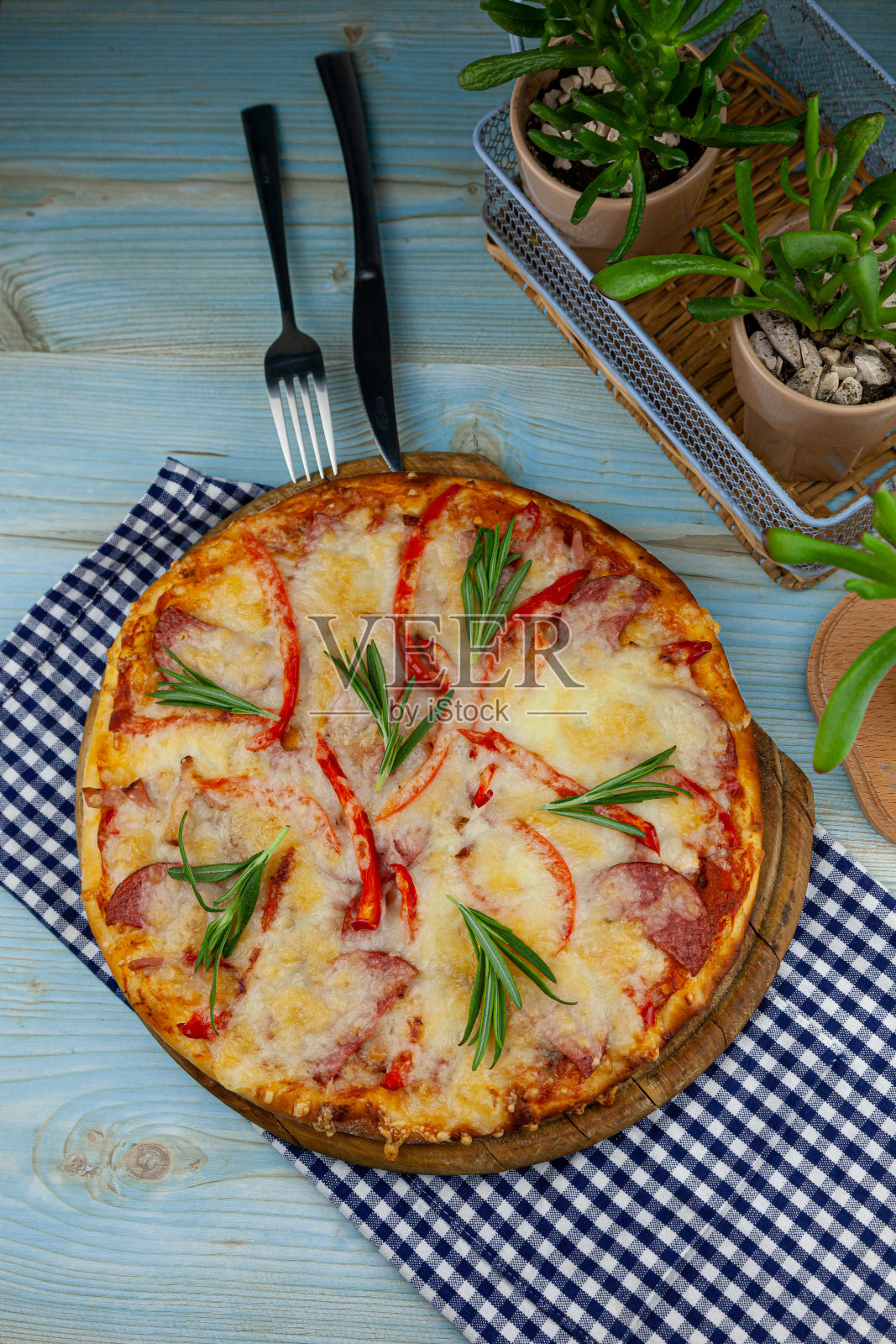 传统的夏威夷披萨放在木托盘上，桌上有方格餐巾。圆披萨有肉，胡椒，香肠，迷迭香和奶酪。自制的。俯视图，蓝色背景和文字的地方照片摄影图片