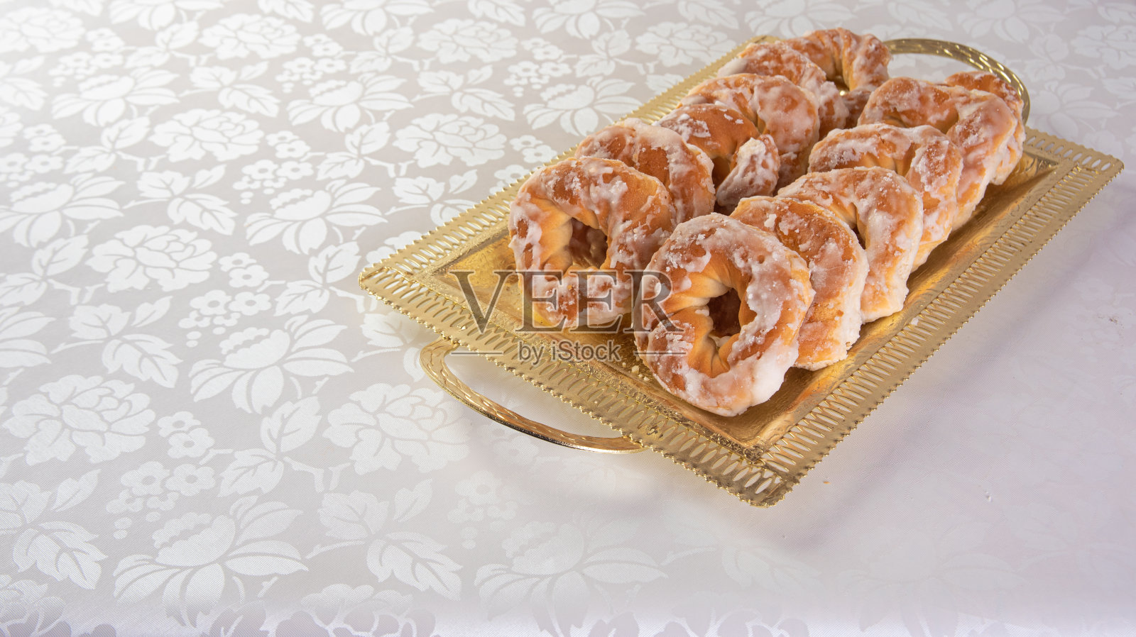 裹着糖衣的甜饼乾放在金色的托盘上，桌上铺着白色的台布，选择性的聚焦。照片摄影图片