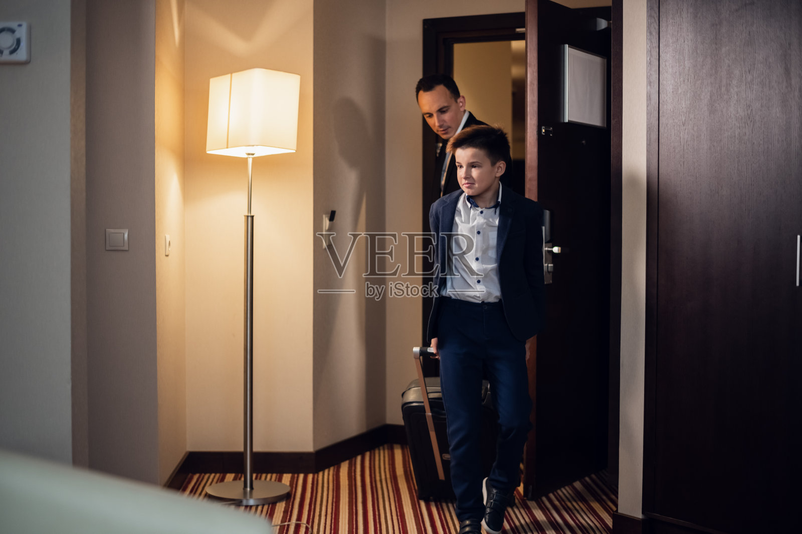 父子俩穿着正装，提着衣箱走进酒店房间照片摄影图片